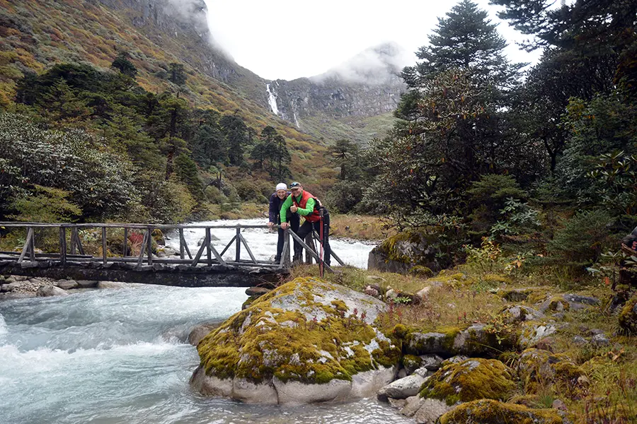 Trekkers crossing a wooden bridge over a mountain river near Uttarey in West Sikkim